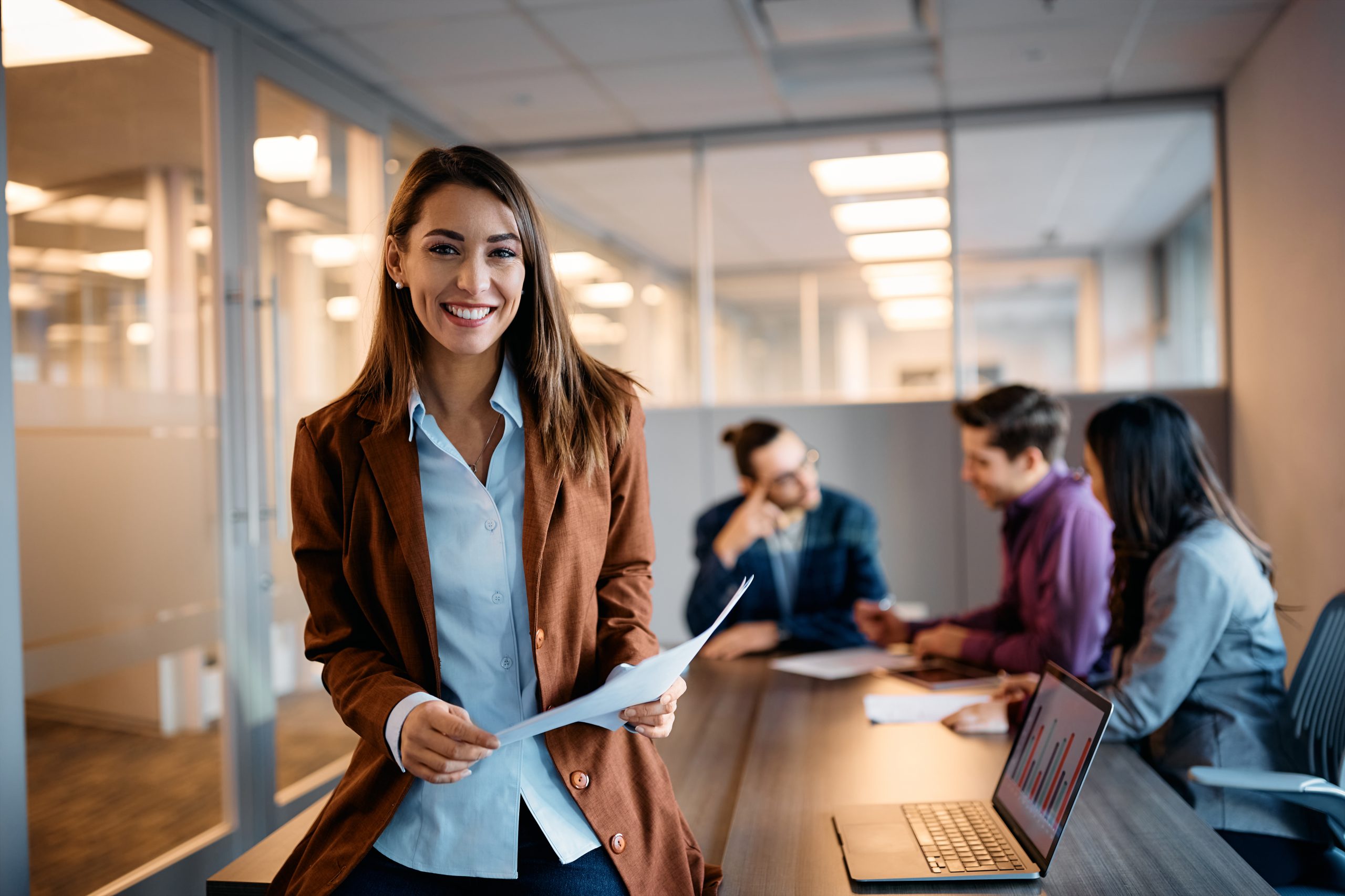 Young happy businesswoman having meeting with her colleagues in office and looking at camera.